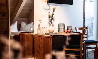A cozy living space with a dining table and wooden shelves. A television hangs on the wall, and the decor feels modern and inviting.