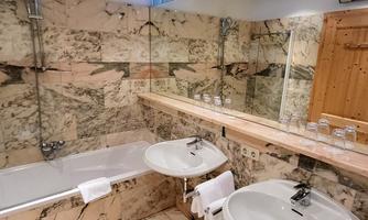 An elegant bathroom with marble walls and modern fixtures. It features a bathtub, two sinks, and a bright, inviting atmosphere.