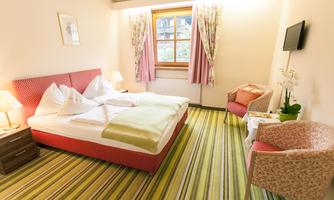 A cozy hotel room with a double bed and fresh, bright colors. There is a comfortable armchair and a large window with curtains.
