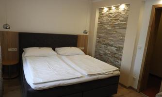 A modern bedroom with a double bed and a decorative stone wall. The walls are bright and the lighting is pleasant.