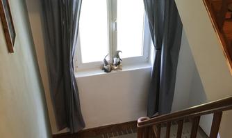 A staircase with a brown railing and mats. Gray curtains hang in front of a window, and light streams in.