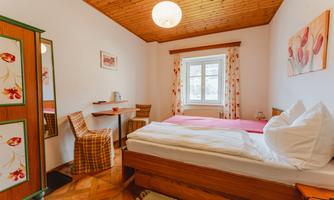 A cozy bedroom with wooden paneling on the ceiling. There is a large bed, a table and chairs, as well as a wardrobe.