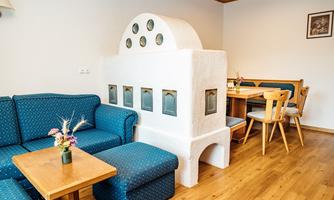 A cozy living area with blue sofas and a wooden table. In the room stands a unique, white fireplace with windows.