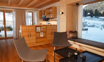 A cozy living space with wooden paneling and large windows that offer a view of a snow-covered landscape. In the center are modern furniture and a small bar.