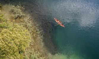 A tranquil lake with clear water and a green shoreline. A small boat with people is floating on the water.