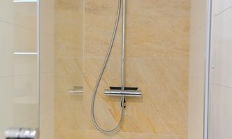 A modern shower with clear glass panels and an elegant, chrome fixture. The walls are designed with bright tiles in sandstone optic.