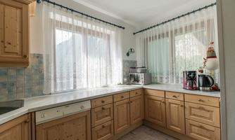 A bright kitchen with wooden cabinets and a large window. On the countertop, there is a kettle and a microwave.