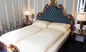 An elegant bedroom with a large, upholstered bed and luxurious subtle colors. The walls are decorated with blue and golden stripes.