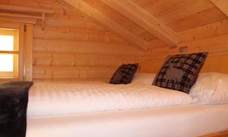 A cozy bedroom with a wooden ceiling and a large bed. On the bed are two pillows with a checked pattern.