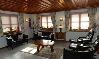 A cozy living room with black leather sofas and a wooden coffee table. There are large windows with curtains and a warm lighting ambiance.