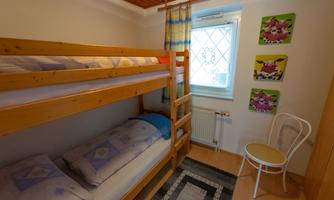 A cozy bedroom with a bunk bed and a comfortable chair. Bright walls and colorful pictures give the room a friendly atmosphere.