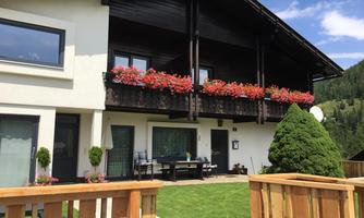 A beautiful house with a balcony adorned with colorful flowers. The garden is neatly maintained and surrounded by green grass.