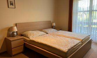 A cozy bedroom with a double bed and two nightstands. Large windows provide plenty of daylight.