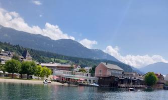 A beautiful lake with clear blue water and a view of the mountains. In the background, buildings and trees can be seen.