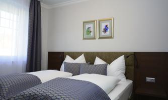 A modern bedroom with two beds and elegant bedding. Two pictures hang on the wall, and the light gently falls through the window.