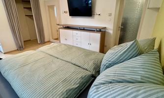 A cozy bedroom with two beds and striped bedding. On the wall, there is a television and a modern dresser.