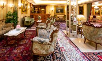 An elegant living room with antique furniture and a richly decorated carpet. Cozy seating areas provide an inviting atmosphere.