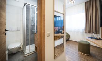 A modern bathroom with a shower and toilet, adjacent to a minimally furnished living area. The space is bright and cozy, with a window and a small table.