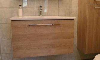 A modern bathroom with a wooden washbasin, a mirror, and bright tiles. The room is clean and well-organized.