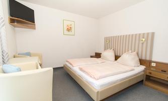 A bright and modern bedroom with two beds and a cozy seating area. A TV hangs on the wall, and there is a decorative picture.