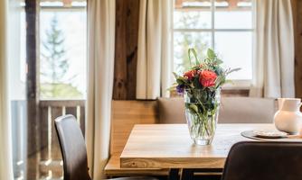 A beautiful table with a flower vase and fresh flowers. In the background, there is a window overlooking nature.