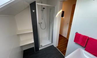 A modern bathroom with a shower cabin and a sink. The walls are light and there is a contrast from the dark tiles and the red towels.