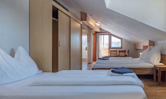 A cozy bedroom with two beds and modern furniture. Light streams through a window, creating an inviting atmosphere.
