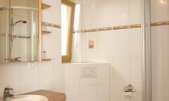 A modern bathroom with bright tiles and a wooden ceiling. It features a sink, a toilet, and a shower cubicle.