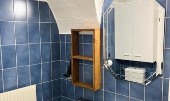 A modern bathroom with blue tiles and a white sink. A mirror and a lighted cabinet are also present.