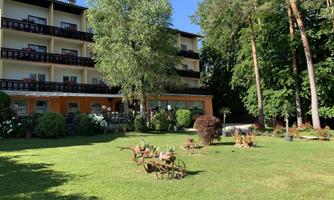 A well-maintained garden with a large lawn and beautiful plants. In the background stands a multi-story building surrounded by trees.