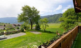 A beautiful landscape with green meadows and mountains in the background. In the foreground, there is a balcony with flowers and a serene atmosphere.