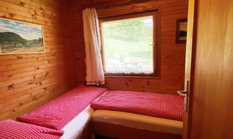 A cozy room with two single beds and red bedding. The wooden interior and the window offer a view of the outdoors.