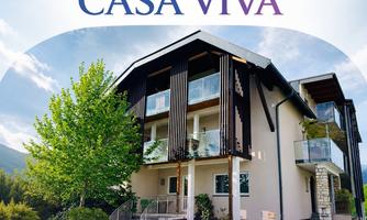 A modern building with large windows and balconies, surrounded by green trees. Above the building is the logo "CASA VIVA".