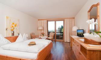 A cozy hotel room with a large double bed and wooden furniture. There is a balcony with a view and a pleasant, bright atmosphere.