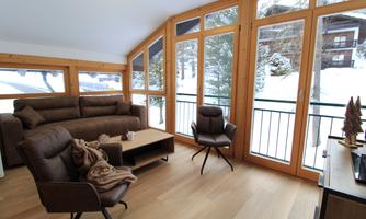 A cozy living space with large windows offering a view of snow-covered trees. The wooden decorative elements give the room a warm atmosphere.
