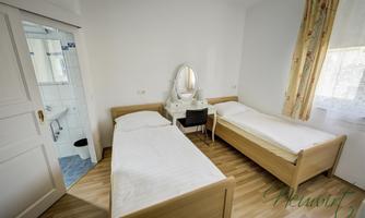 A simple room with two single beds, a table, and a mirror. In the background, a bathroom is visible.