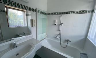 A modern bathroom with a bathtub and a shower. The walls are tiled in white and there is a window for natural light.