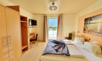 A bright room with a double bed and a TV. Large windows offer a view outside and the decor is modern and friendly.
