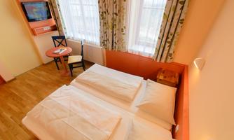 A cozy room with two beds and a small table.  
Bright windows with curtains create a pleasant atmosphere.