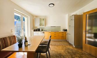 A modern kitchen with a wooden table and chairs.  
Lots of light enters the room through large windows.
