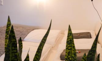 A cozy bedroom with a large bed and plants in the foreground. A decorative lamp with the inscription "LOVE" hangs on the wall.