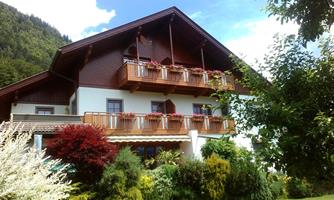A charming house with a wooden roof and several balconies. Surrounded by lush greenery and colorful plants.