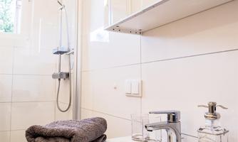 A modern bathroom with a sink, a towel, and a shower. The walls are brightly tiled and the lighting is pleasant.