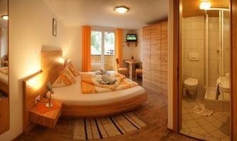 A bright room with a round bed and orange curtains. In the background, there is a small bathroom with a shower.