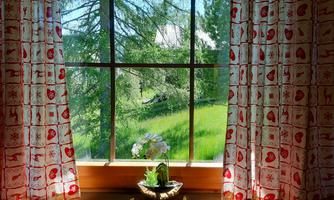 A window view with colorful curtains showing a green garden with trees. On the windowsill, there is a potted plant.