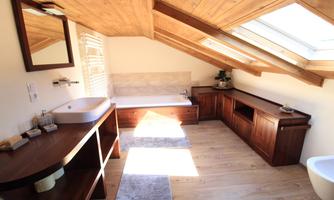 A modern bathroom with wood paneling and skylights. There is a bathtub, a sink, and stylish furniture.