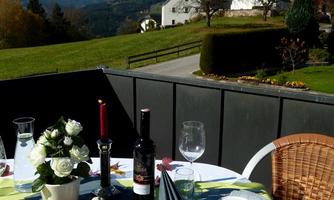 A beautifully set table on a terrace overlooking a picturesque church and the surrounding hills. The scene conveys a cozy and inviting atmosphere.