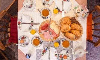 A beautifully set breakfast table with rolls, cold cuts, eggs, and various drinks. The table is lovingly decorated and invites you to enjoy.