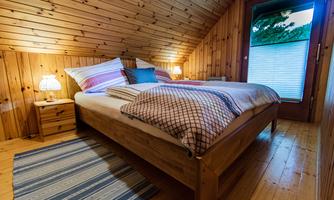 A cozy bedroom with wood paneling and a large bed.  
Next to the bed are nightstands with lamps and there is a window with a view.