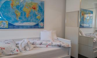 A simple bedroom with a white single bed and a world map on the wall. There is a wardrobe with a mirror and bright bedding.